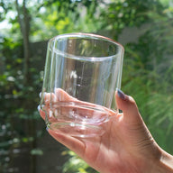 Clear glass held in a hand with a blurred green outdoor background