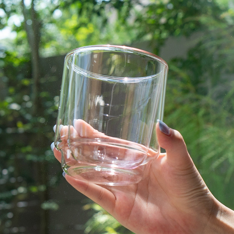 Clear glass held in a hand with a blurred green outdoor background