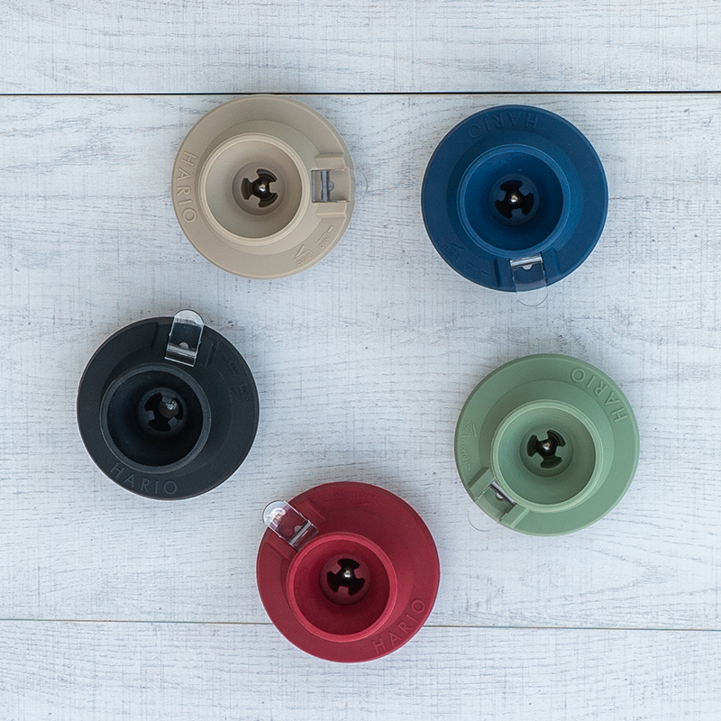 A collection of five switch bases in different colors (black, blue, beige, green, and red) displayed on a wooden surface.